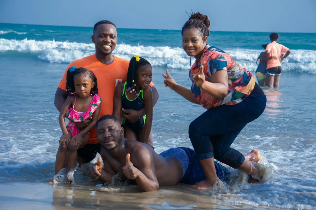 Black British family of five enjoying beach holiday in turquoise waters after booking with holiday installment payment plan
